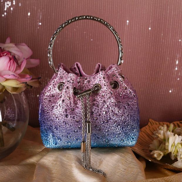 Sparkly purple and blue handbag with decorative handle and keychain on a soft surface.